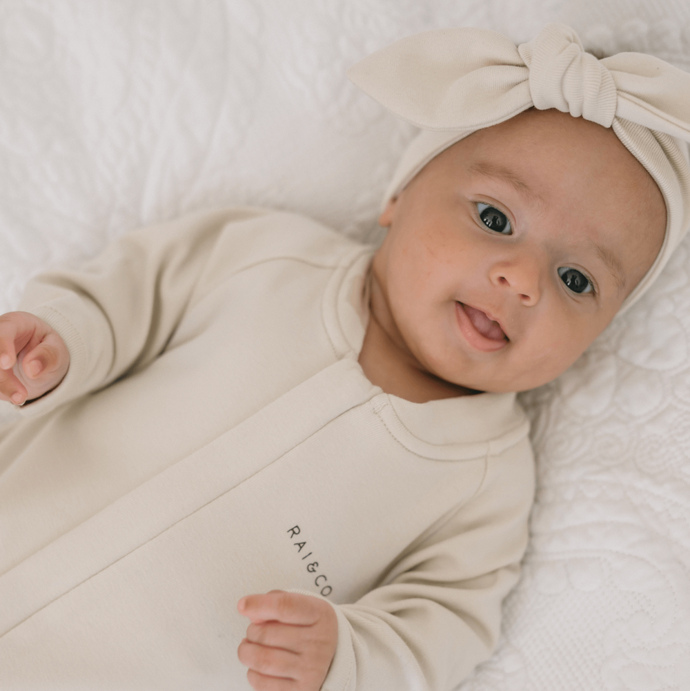 Baby wearing a beige outfit and headband on a white background